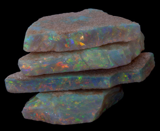 Four stacked rough opal pieces showing multicoloured play-of-colour against a black background.