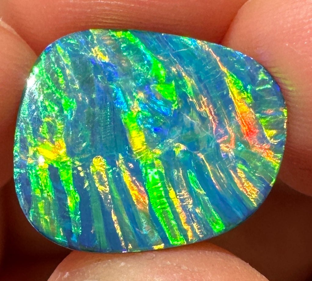 Lambina opal doublet held between fingers, displaying vivid blue, green, yellow and orange play-of-colour.